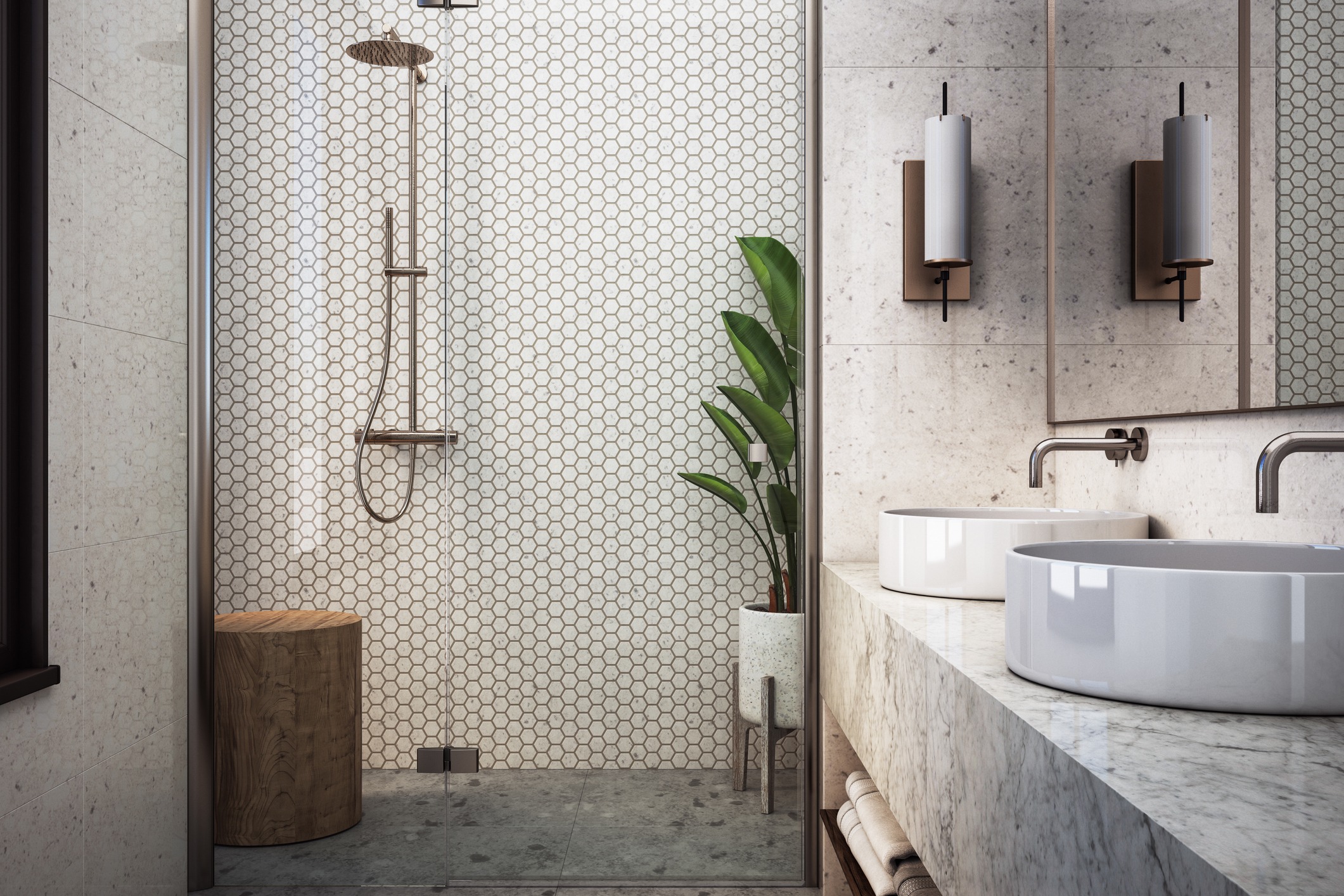 Modern bathroom with a walk-in shower featuring hexagonal tile, a wooden stool, and a potted plant. Double sinks rest on a marble counter with cylindrical wall-mounted lights above. Warm, neutral tones create a sleek, inviting ambiance.